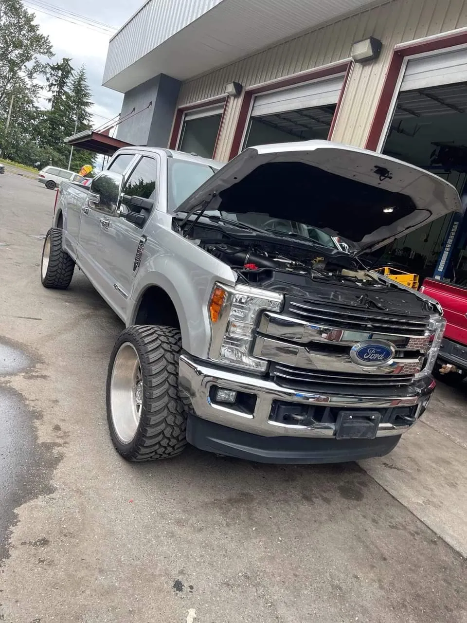 A silver Ford Super Duty with the hood up, outside the bays