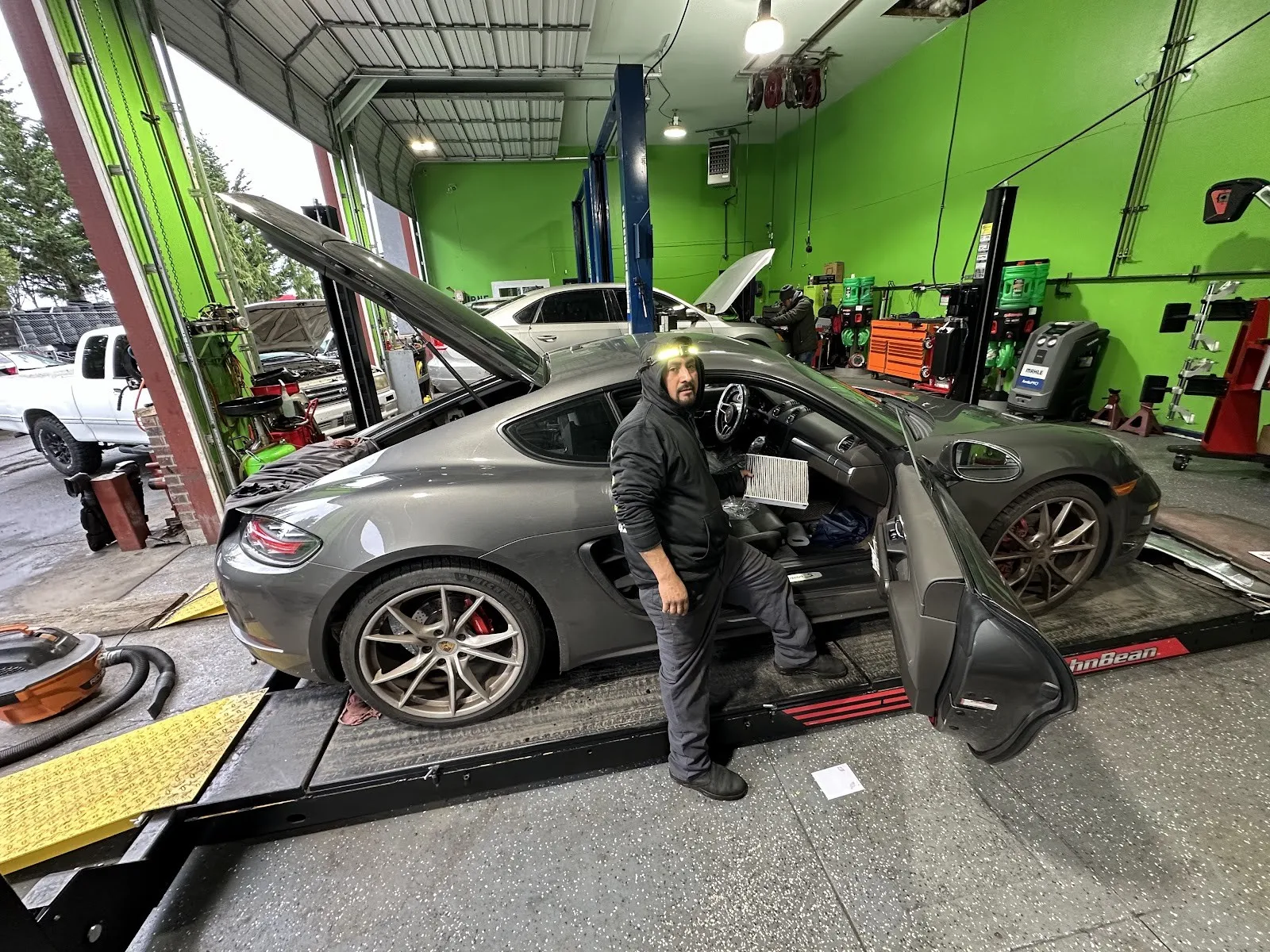 A gray Porsche Cayman on the alignment rack, a technician beside it