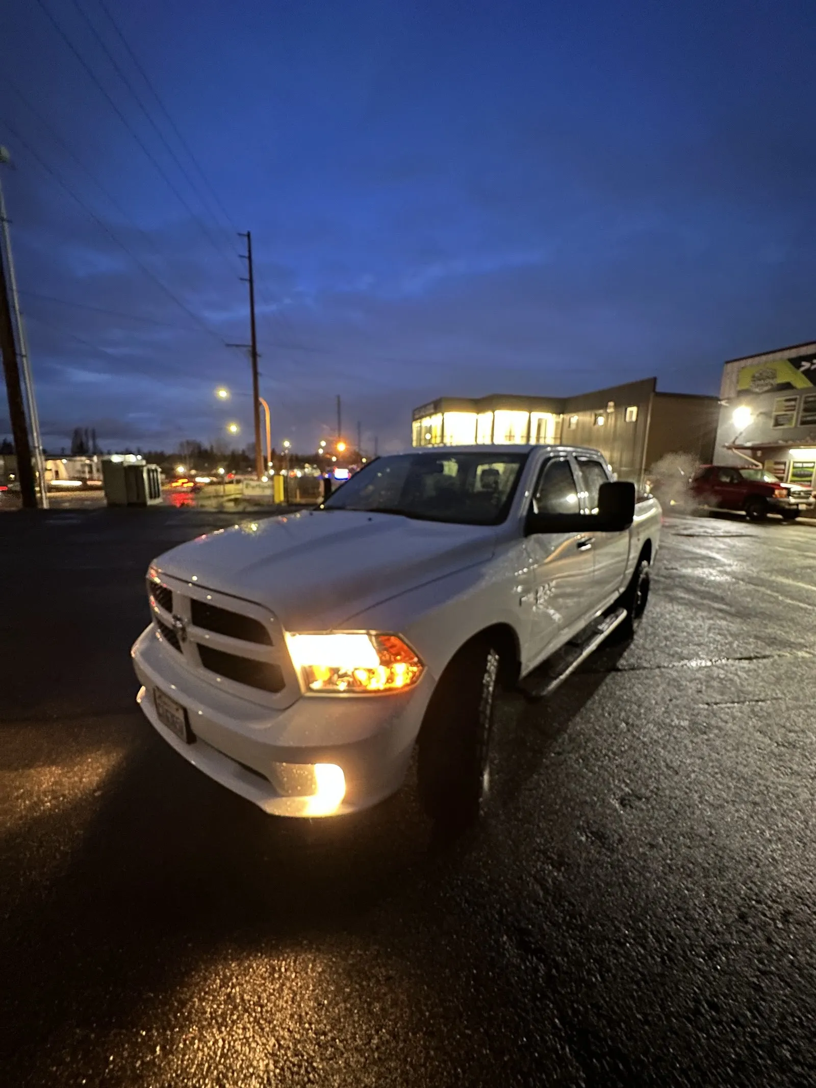 A white Ram pickup in the lot at dusk, headlights on